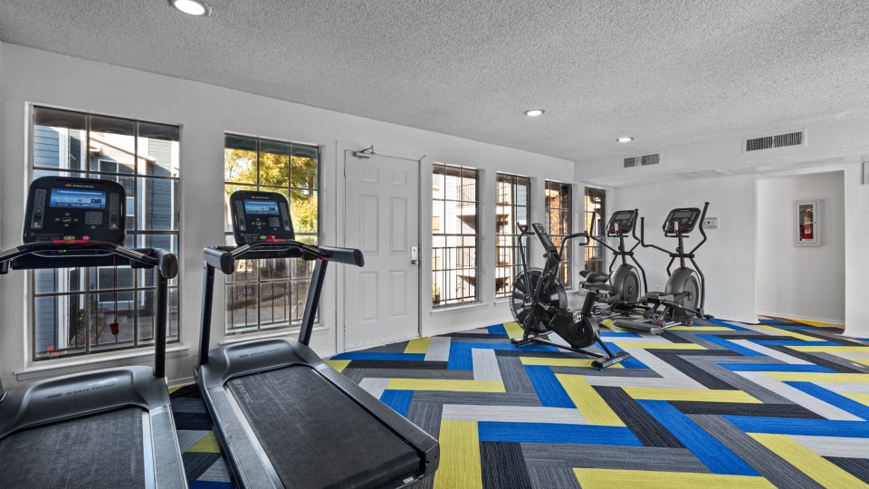 a gym room with tread machines and a blue and yellow checkered floor at The Landing at McCallum