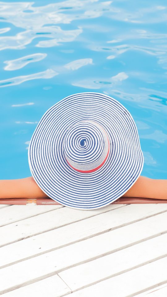 woman leaning on white concrete surface beside swimming pool during daytime